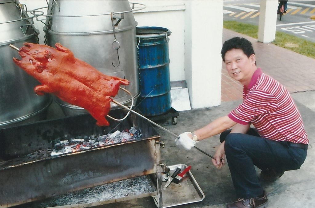A whole pig being turned by hand over a charcoal fire
