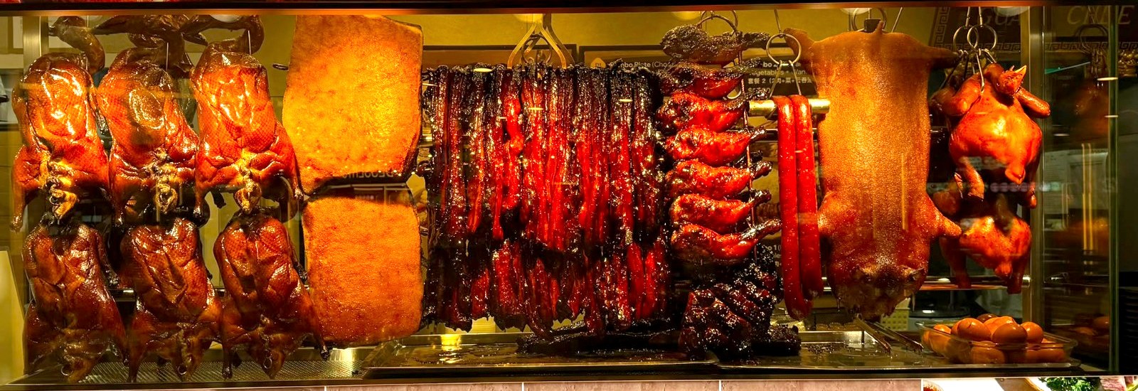 Crispy roast pork, char siew, soya chickens and sausage hanging in the warmer at a Guan Chee counter
